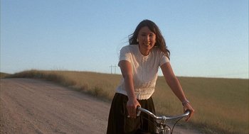 Movie still from “Napoleon Dynamite” (2004), directed by Jared Hess – A woman riding a bike down a dirt road; Medium shot, Low angle