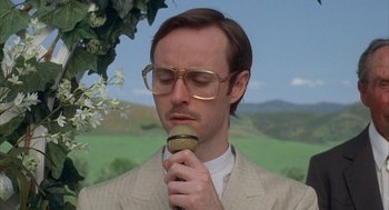 Movie still from “Napoleon Dynamite” (2004), directed by Jared Hess – A man with glasses is holding a microphone up to his mouth; Close Up shot, Low angle