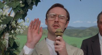 Movie still from “Napoleon Dynamite” (2004), directed by Jared Hess – A man in a beige suit is holding a microphone; Close Up shot, Low angle