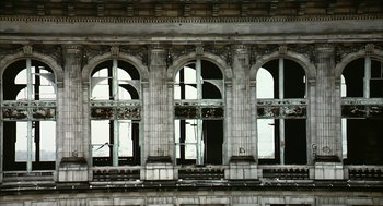 Movie still from “Naqoyqatsi” (2002), directed by Godfrey Reggio – An old building has three arched windows on it's side; Extreme Wide shot, Low angle