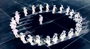 Movie still from “Naqoyqatsi” (2002), directed by Godfrey Reggio – A group of people that are standing in a circle; Extreme Wide shot, Overhead angle