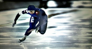 Movie still from “Naqoyqatsi” (2002), directed by Godfrey Reggio – A man in a blue suit is skating on ice; Medium shot, Overhead angle