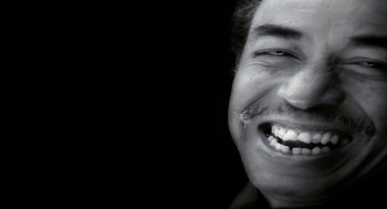 Movie still from “Naqoyqatsi” (2002), directed by Godfrey Reggio – A black and white photo of a man smiling; Extreme Close Up shot, Low angle