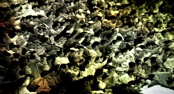 Movie still from “Naqoyqatsi” (2002), directed by Godfrey Reggio – A large group of people sitting in a room together; Extreme Wide shot, Overhead angle