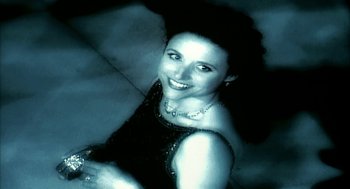 Movie still from “Naqoyqatsi” (2002), directed by Godfrey Reggio – A woman in a black dress smiling for the camera; Close Up shot, High angle