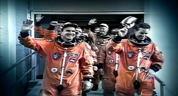 Movie still from “Naqoyqatsi” (2002), directed by Godfrey Reggio – A group of men in orange suits and hats; Medium shot, Low angle