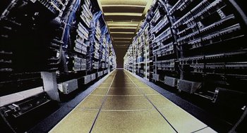 Movie still from “Naqoyqatsi” (2002), directed by Godfrey Reggio – A long hallway with many rows of computer equipment on the walls; Extreme Close Up shot, Overhead angle