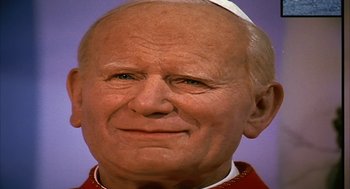 Movie still from “Naqoyqatsi” (2002), directed by Godfrey Reggio – A wax statue of a man wearing a priest's outfit; Extreme Close Up shot, High angle