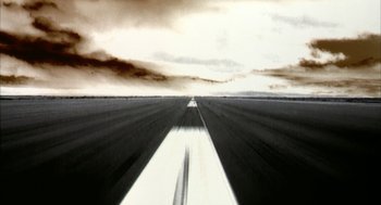 Movie still from “Naqoyqatsi” (2002), directed by Godfrey Reggio – An image of an empty runway in the middle of a cloudy day; Extreme Wide shot, Low angle