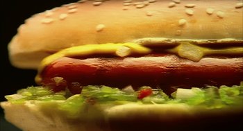Movie still from “Naqoyqatsi” (2002), directed by Godfrey Reggio – A hot dog on a hamburger bun; Extreme Close Up shot, Overhead angle