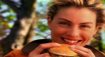 Movie still from “Naqoyqatsi” (2002), directed by Godfrey Reggio – A person eating a hamburger; Extreme Close Up shot, Overhead angle