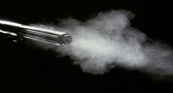 Movie still from “Naqoyqatsi” (2002), directed by Godfrey Reggio – A gun that has been fired with smoke coming out of it; Extreme Close Up shot, Low angle