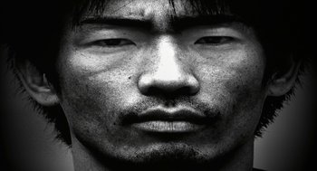 Movie still from “Naqoyqatsi” (2002), directed by Godfrey Reggio – Black and white photograph of a man's face; Extreme Close Up shot, Overhead angle