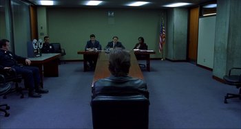 Movie still from “Narc” (2002), directed by Joe Carnahan – Three people are sitting at a long wooden table in a conference room; Wide shot, Over the shoulder angle