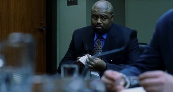 Movie still from “Narc” (2002), directed by Joe Carnahan – A man sitting at a table holding a piece of paper; Medium shot, Over the shoulder angle