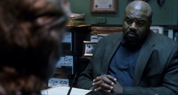 Movie still from “Narc” (2002), directed by Joe Carnahan – A man sitting at a table in front of papers; Medium shot, Over the shoulder angle