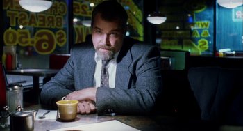 Movie still from “Narc” (2002), directed by Joe Carnahan – A man sitting at a table with a cup of coffee in front of him; Medium shot, Low angle