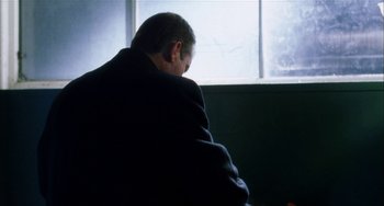 Movie still from “Narc” (2002), directed by Joe Carnahan – A man sitting in front of a large window; Medium shot, Low angle