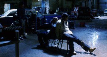 Movie still from “Narc” (2002), directed by Joe Carnahan – A man and a woman sitting on a chair in a garage; Wide shot, High angle