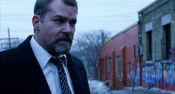 Movie still from “Narc” (2002), directed by Joe Carnahan – A man in a suit and tie standing in front of a building; Close Up shot, Low angle