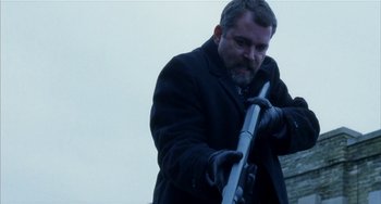 Movie still from “Narc” (2002), directed by Joe Carnahan – A man in a black coat holding a rifle; Medium shot, Low angle