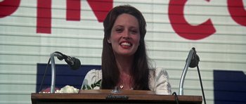 Movie still from “Nashville” (1975), directed by Robert Altman – A woman smiles at the camera while sitting in front of a microphone; Close Up shot, Low angle