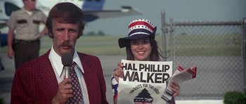 Movie still from “Nashville” (1975), directed by Robert Altman – A man and a woman standing next to each other holding a sign; Medium shot, Low angle