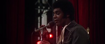 Movie still from “Nashville” (1975), directed by Robert Altman – A man holding a microphone while standing in front of a microphone; Close Up shot, Low angle