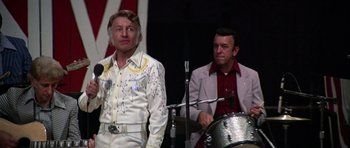 Movie still from “Nashville” (1975), directed by Robert Altman – Two men are performing on a stage with a drum; Medium shot, Low angle