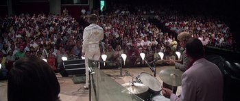 Movie still from “Nashville” (1975), directed by Robert Altman – A crowd of people watching a man in a white suit sing; Wide shot, Low angle