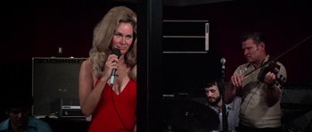 Movie still from “Nashville” (1975), directed by Robert Altman – A woman in a red dress is holding a microphone; Medium shot, Over the shoulder angle