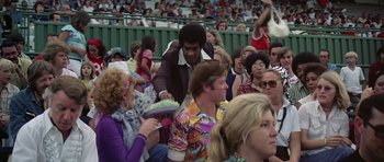 Movie still from “Nashville” (1975), directed by Robert Altman – A crowd of people sitting and standing in front of a fence; Medium shot, Over the shoulder angle