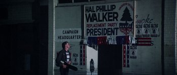 Movie still from “Nashville” (1975), directed by Robert Altman – A man holding a skateboard in front of a political sign; Wide shot, Low angle