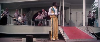Movie still from “Nashville” (1975), directed by Robert Altman – A man standing on top of a rope next to another man; Wide shot, Low angle