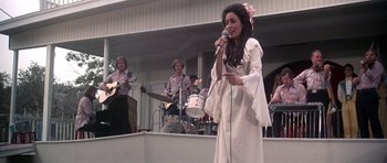 Movie still from “Nashville” (1975), directed by Robert Altman – A woman singing into a microphone in front of a group of people; Medium shot, Low angle