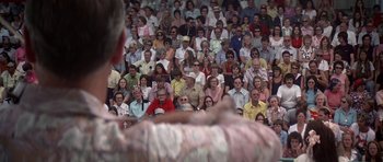 Movie still from “Nashville” (1975), directed by Robert Altman – A crowd of people sitting and standing in front of a man; Medium shot, High angle