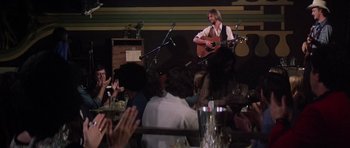 Movie still from “Nashville” (1975), directed by Robert Altman – A man playing guitar in front of an audience at an event; Wide shot, Over the shoulder angle