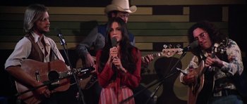 Movie still from “Nashville” (1975), directed by Robert Altman – A woman holding a microphone while standing next to a man playing a guitar; Medium shot, Low angle