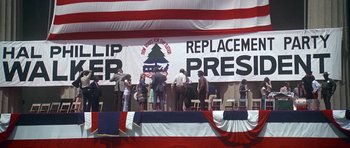 Movie still from “Nashville” (1975), directed by Robert Altman – A group of people standing on top of a stage under a banner; Extreme Wide shot, High angle