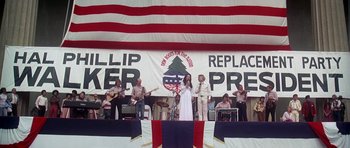 Movie still from “Nashville” (1975), directed by Robert Altman – A group of people on a stage with a flag in the background; Wide shot, High angle