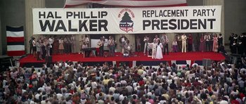 Movie still from “Nashville” (1975), directed by Robert Altman – A crowd of people sitting and standing in front of a building; Wide shot, Overhead angle