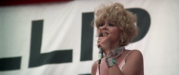 Movie still from “Nashville” (1975), directed by Robert Altman – A woman with blonde curly hair is holding a microphone; Close Up shot, Low angle