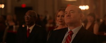 Movie still from “National Champions” (2021), directed by Ric Roman Waugh – A man in a suit and a red and white striped tie; Medium shot, Low angle