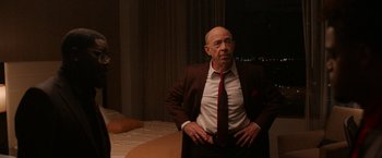 Movie still from “National Champions” (2021), directed by Ric Roman Waugh – An older man wearing a suit and tie standing next to a bed; Medium shot, Over the shoulder angle
