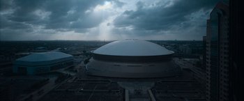 Movie still from “National Champions” (2021), directed by Ric Roman Waugh – An aerial view of a large stadium with a cloudy sky; Extreme Wide shot, Low angle