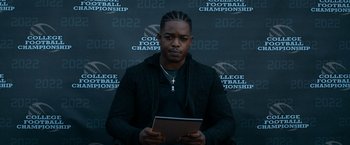 Movie still from “National Champions” (2021), directed by Ric Roman Waugh – A man holding a tablet in front of a wall; Medium shot, Over the shoulder angle