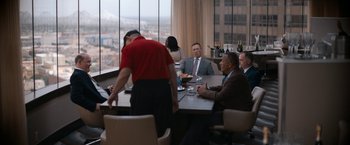 Movie still from “National Champions” (2021), directed by Ric Roman Waugh – A group of people sitting at a table in front of a large window; Wide shot, Over the shoulder angle