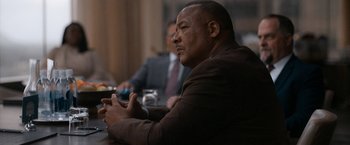 Movie still from “National Champions” (2021), directed by Ric Roman Waugh – A man sitting at a table with a cell phone in his hand; Medium shot, Over the shoulder angle