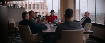 Movie still from “National Champions” (2021), directed by Ric Roman Waugh – A group of men sitting at a table in front of a window; Wide shot, Over the shoulder angle