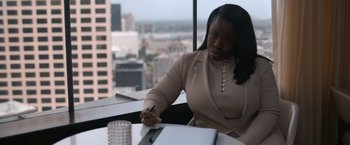 Movie still from “National Champions” (2021), directed by Ric Roman Waugh – A woman sitting at a table with a pen in her hand; Medium shot, High angle